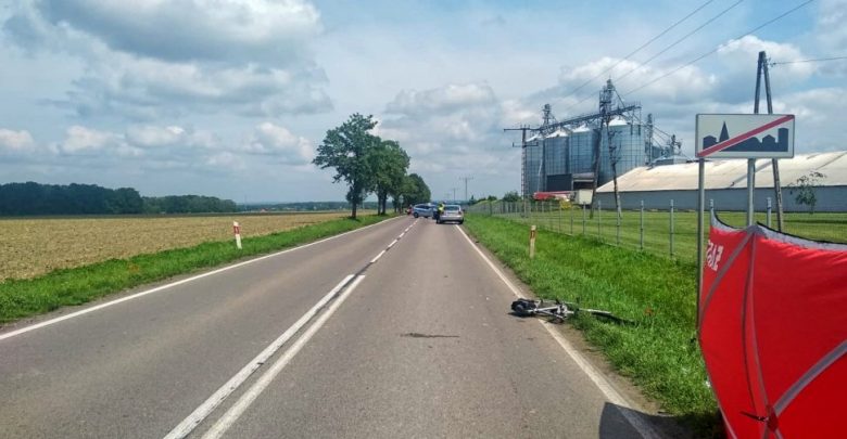 Droga powiatowa, w tle policyjny radiowóz i samochód marki volvo, na pierwszym planie leżący na asfalcie rower