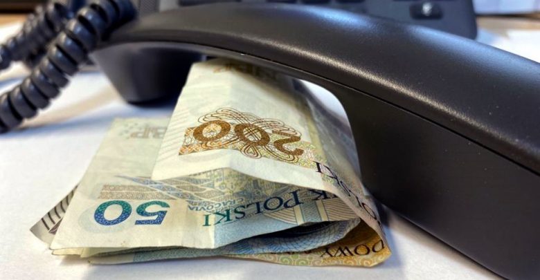 słuchawka telefonu leży na stoliku przy niej banknoty pieniędzy, w tle telefon z klawiaturą