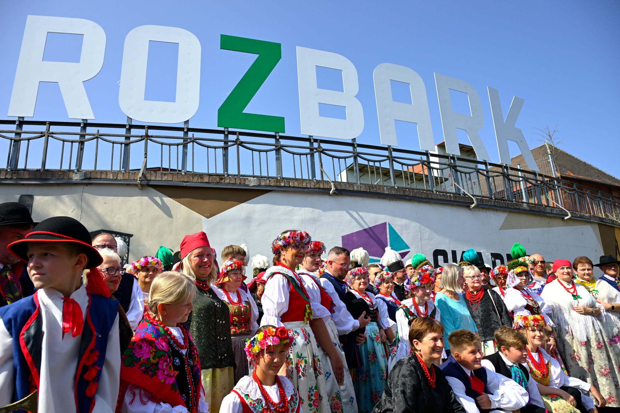 zbiór pamiątek Rozbark, grupa ludzi pozuje do zdjęcia, nad nimi duży napis Rozbark, w grupie kilka osób w strojach ludowych