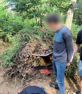 Zatrzymanie poszukiwanego w lesie - zatrzymany mężczyzna w tle szałas z paproci