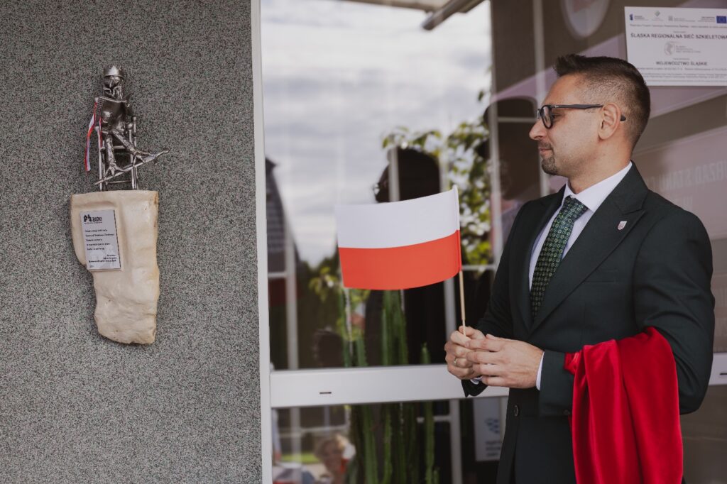 miniaturowa rzeźba obok mężczyzna z flagą biało-czerwoną