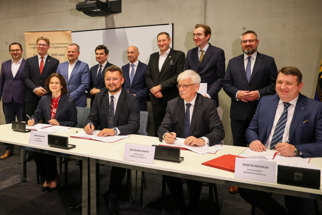 Grupa osób przy stole podpisuje porozumienie - umowę